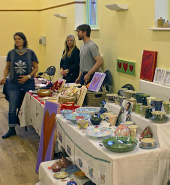Two marketplace stalls selling art and pottery, with stallholders behind